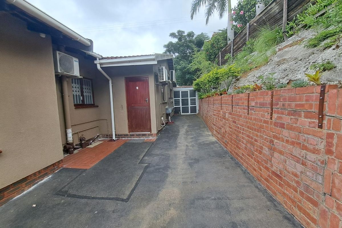 Rear exterior view showing a paved driveway, brick retaining wall, and building access points with installed air conditioning units.