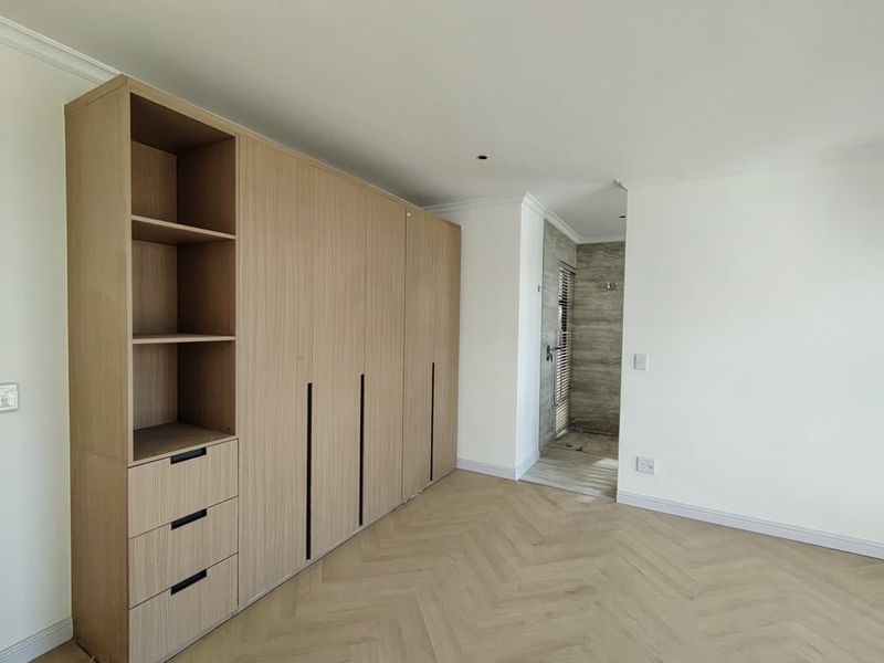 Modern bedroom featuring light wood built-in cupboards, herringbone flooring, and direct access to an en-suite bathroom with stone-look tiling.