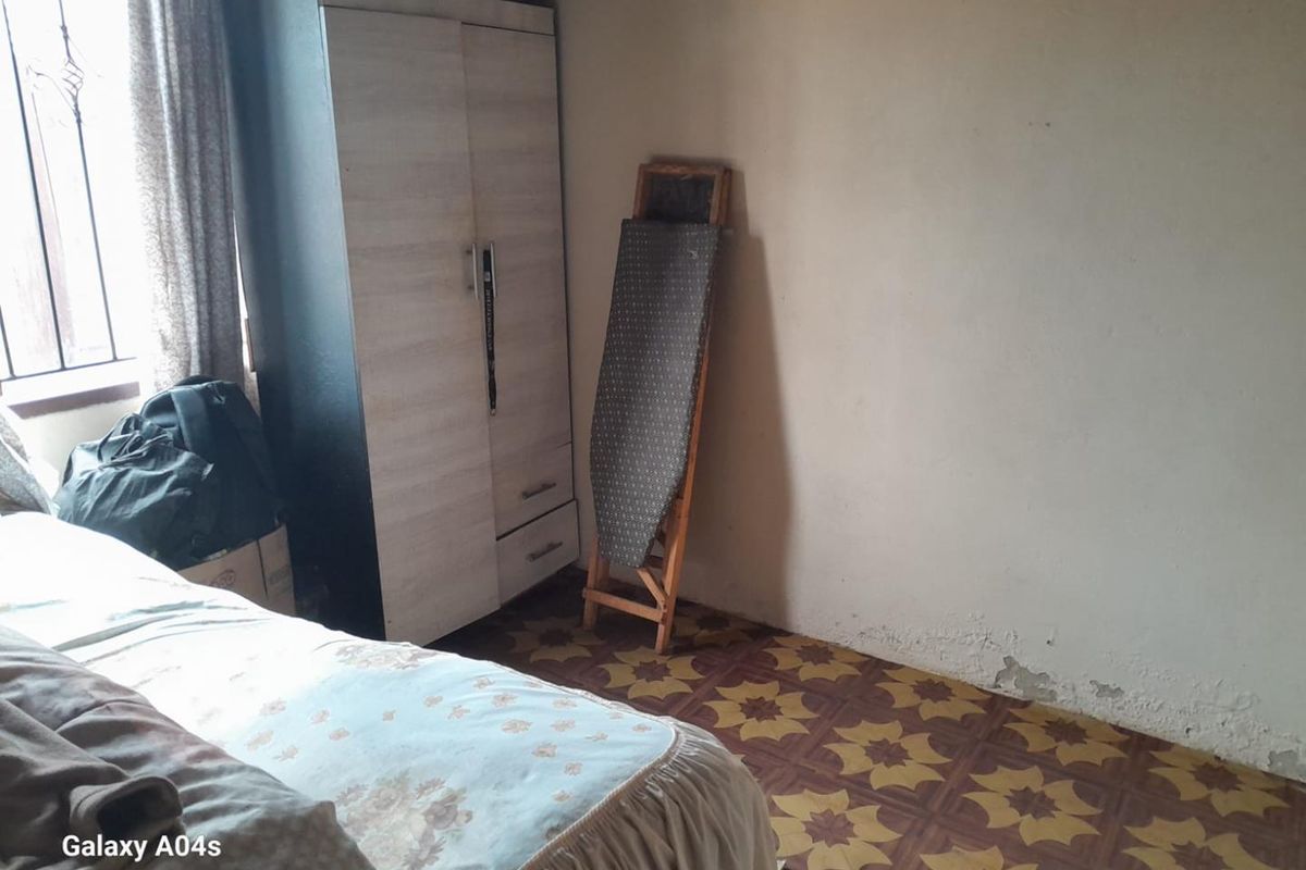 A bedroom featuring patterned vinyl flooring and visible wall surface deterioration, requiring maintenance and cosmetic updates.