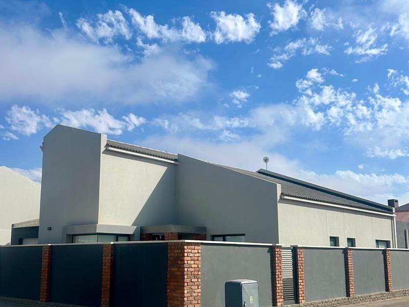 Front exterior view of a modern house featuring a contemporary grey facade, tiled roof, and a secure perimeter wall with brick detailing.