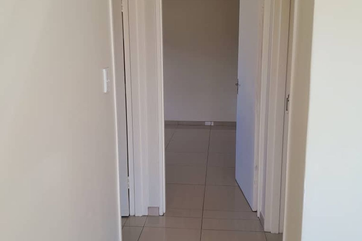 A clean, neutral-toned hallway featuring tiled flooring and multiple internal doorways leading to adjacent rooms.