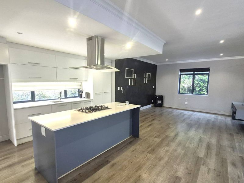 Spacious open-plan living area featuring a modern kitchen with a central island, gas hob, extractor fan, and sleek laminate flooring throughout.