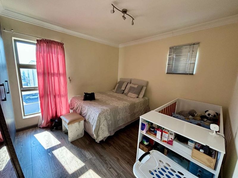A functional bedroom featuring laminate flooring, ceiling coving, and natural light through aluminium-framed windows.