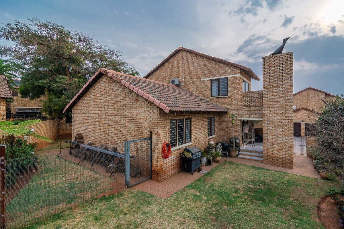 Rear view of a face-brick townhouse featuring a tiled roof, chimney stack, and a private garden area with paved pathways.