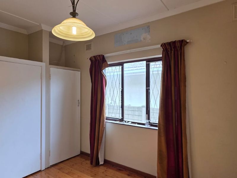 A vacant bedroom featuring timber flooring, built-in cupboards, and an air conditioning unit, requiring minor cosmetic repairs to the wall surfaces.