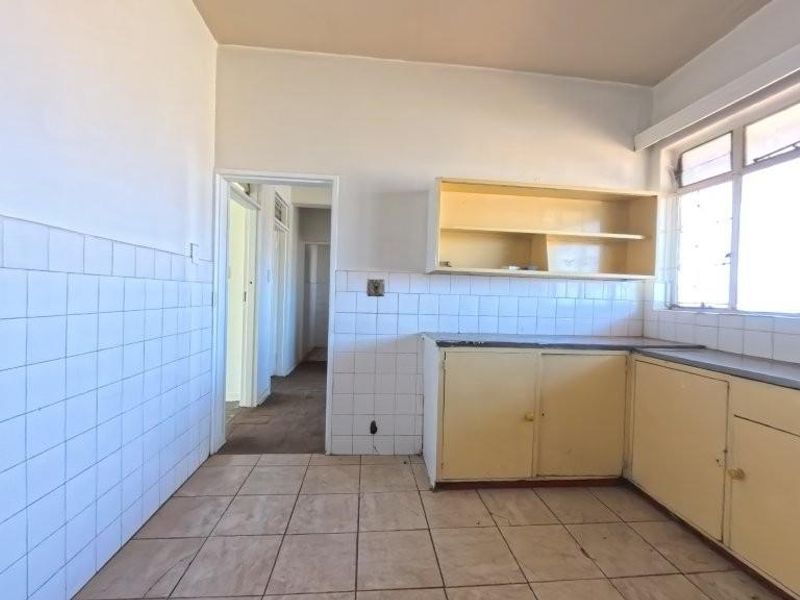 An empty, dated kitchen featuring tiled flooring, tiled splashbacks, and original built-in cabinetry, offering a blank canvas for renovation.