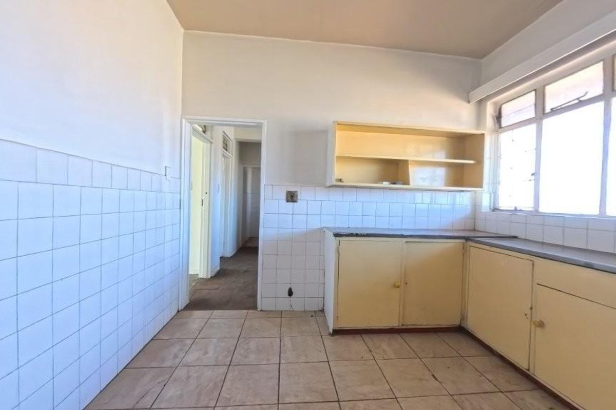 An empty, dated kitchen featuring tiled flooring, tiled splashbacks, and original built-in cabinetry, offering a blank canvas for renovation.