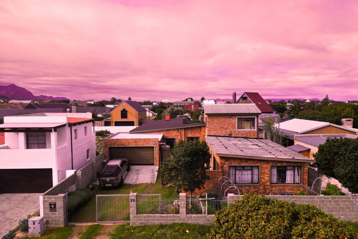 Aerial view of a residential property featuring a brick exterior, metal roofing, and a private driveway within a suburban neighborhood setting.