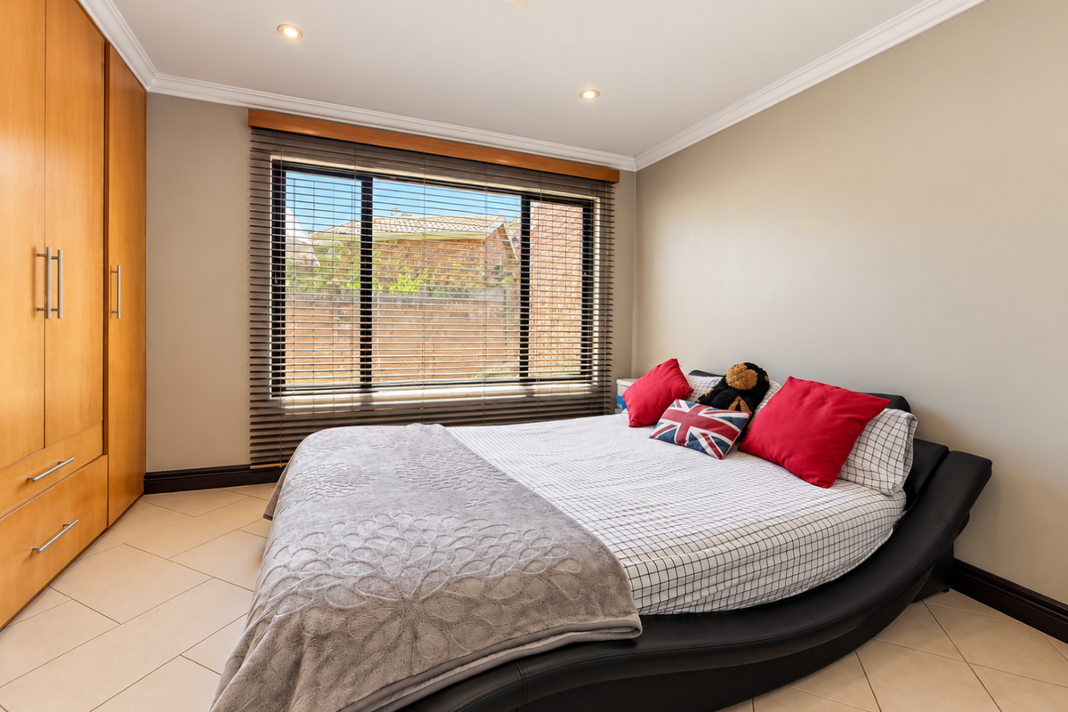 A well-maintained bedroom featuring tiled flooring, built-in wooden cabinetry, recessed lighting, and large windows with venetian blinds.