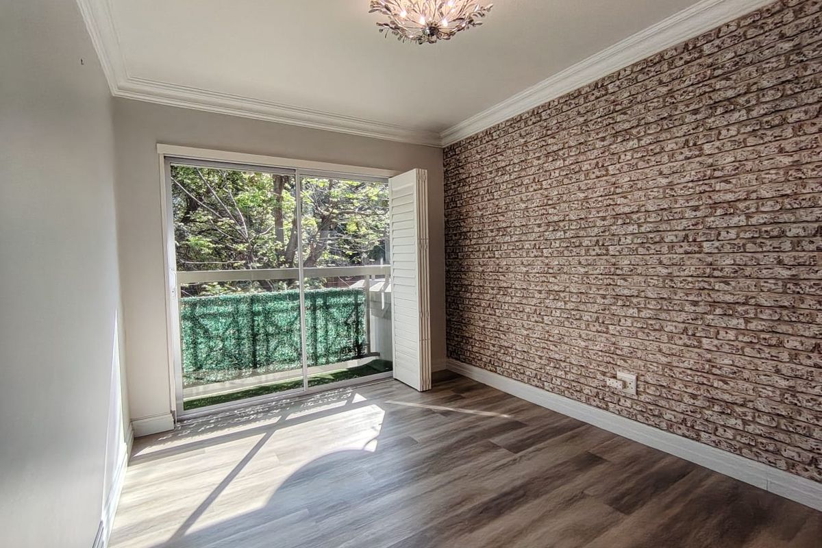 A bright, empty bedroom featuring modern laminate flooring, a decorative faux brick accent wall, and sliding glass doors opening onto a private balcony.