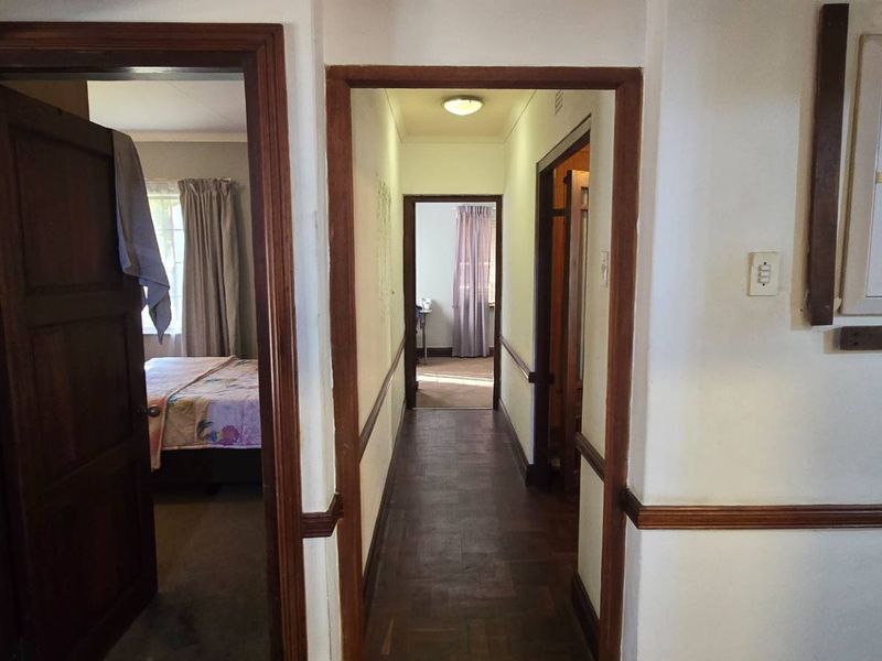 A central hallway featuring parquet flooring, wooden door frames, and a wall-mounted electrical distribution board, providing access to multiple rooms.