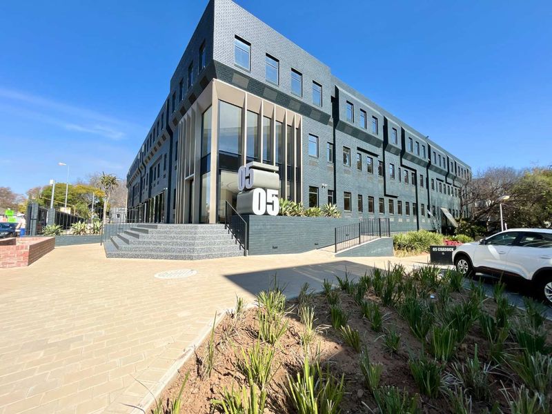 Modern multi-story office building featuring a dark brick facade, prominent glass entrance, and well-maintained paved exterior grounds.