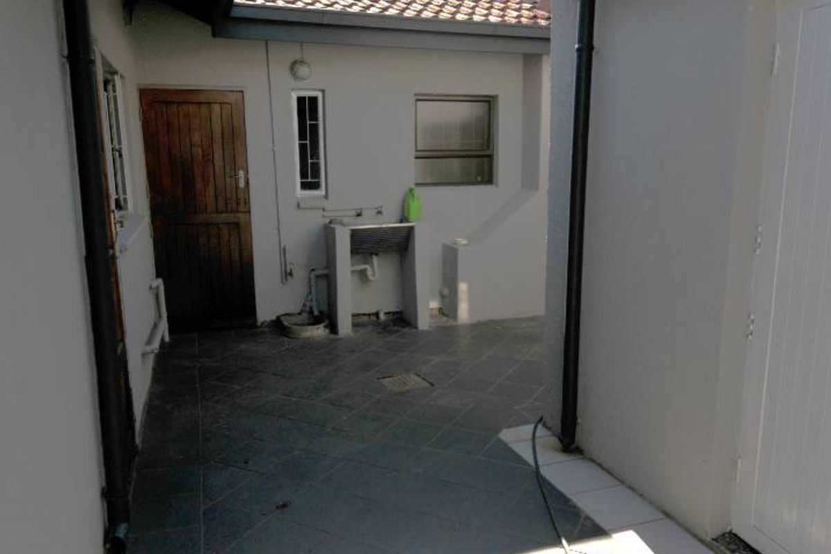 A functional outdoor utility courtyard featuring tiled flooring, a built-in wash basin, and access to multiple building entry points.