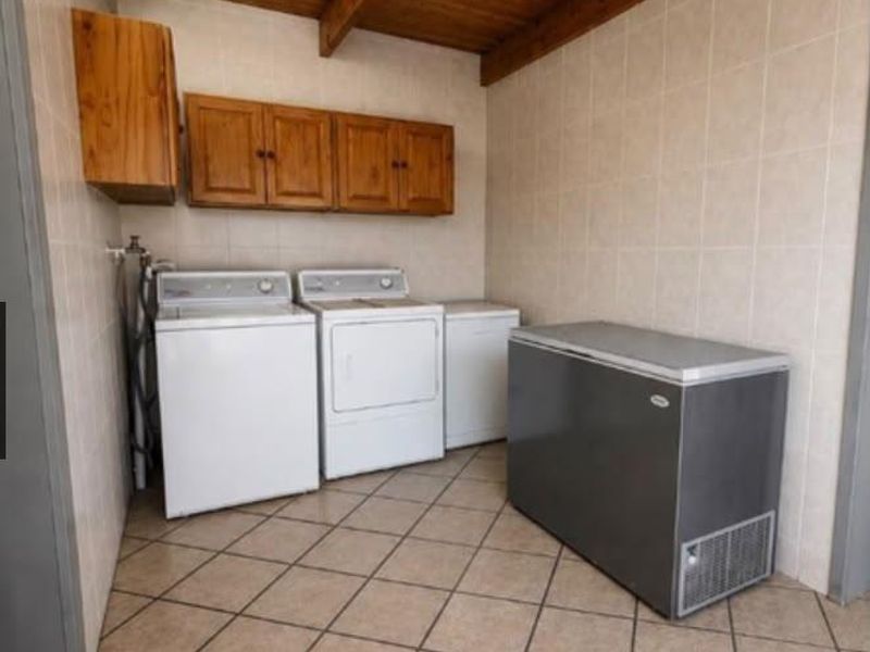 Functional laundry room featuring tiled walls and flooring, exposed timber beam ceiling, and built-in wooden cabinetry for storage.