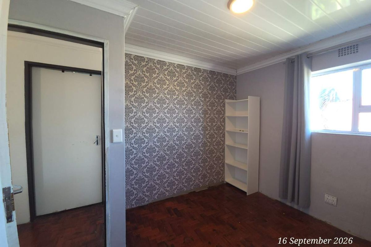 A bedroom featuring parquet flooring, a tongue and groove ceiling, and a feature wallpaper wall, presenting a functional space ready for personalization.