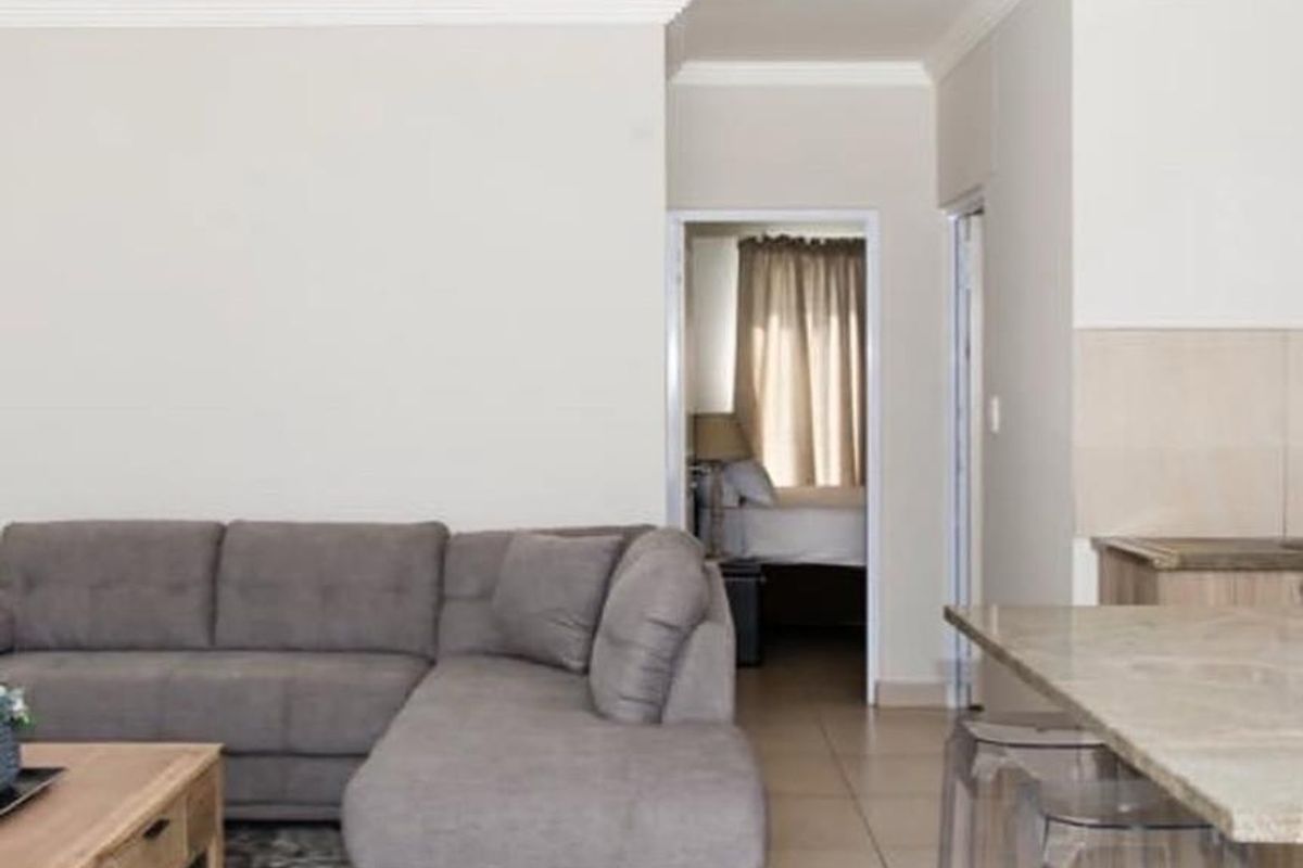 Open plan living area featuring tiled flooring, stone kitchen countertops, and neutral wall finishes with access to an adjacent bedroom.
