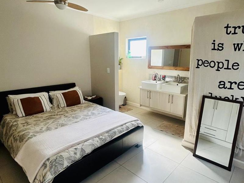 A spacious bedroom featuring an open-plan en-suite bathroom with a double vanity, tiled flooring, and a ceiling fan.