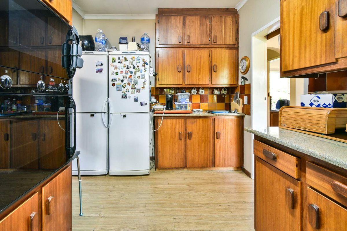 A dated kitchen featuring wood-veneer cabinetry, a tiled backsplash, and built-in oven, offering a functional layout with potential for modern renovation.