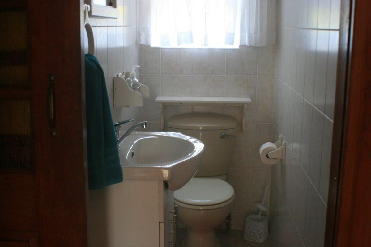 A compact bathroom featuring a wall-mounted basin, a standard toilet, and full-height wall tiling.