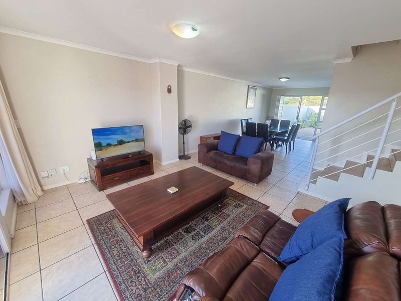Spacious open-plan living and dining area featuring neutral tiled flooring, a staircase with a modern metal railing, and direct access to the rear patio.