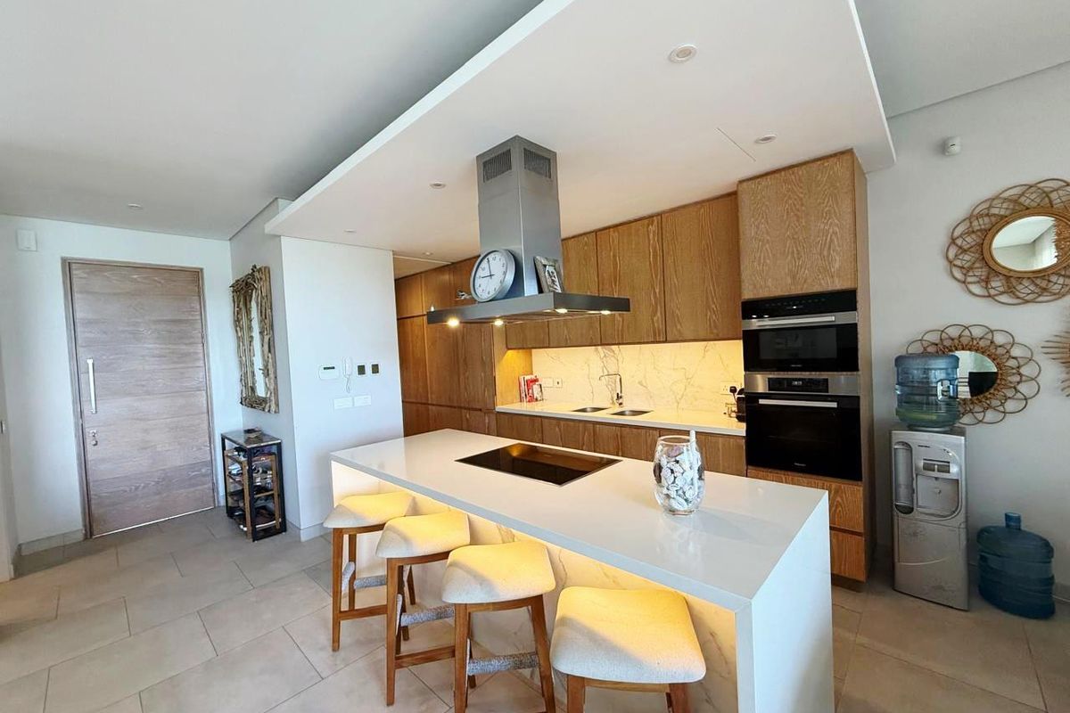 Modern kitchen featuring a large central island with integrated hob, sleek wooden cabinetry, built-in appliances, and high-quality stone countertops.