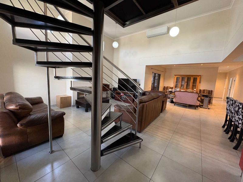 Spacious open-plan living area featuring a modern spiral staircase, tiled flooring, and a split-system air conditioner, offering a versatile layout for dining and relaxation.