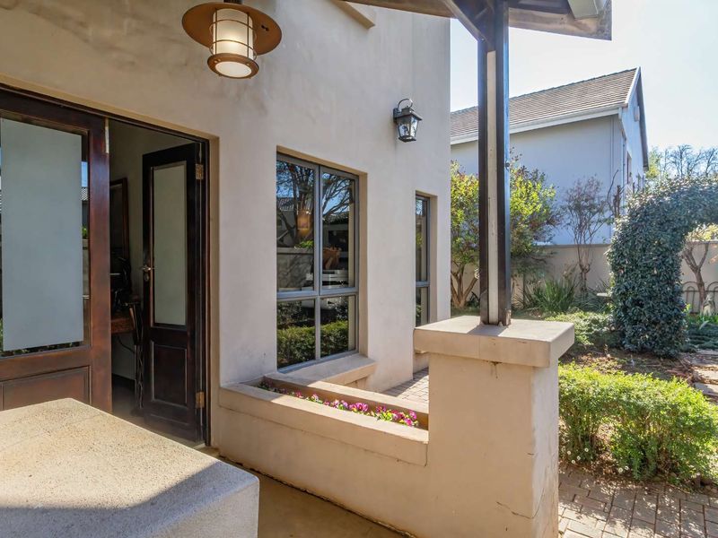 A covered patio area featuring paved flooring, a built-in planter box, and timber-framed glass doors leading into the home, overlooking a landscaped garden.