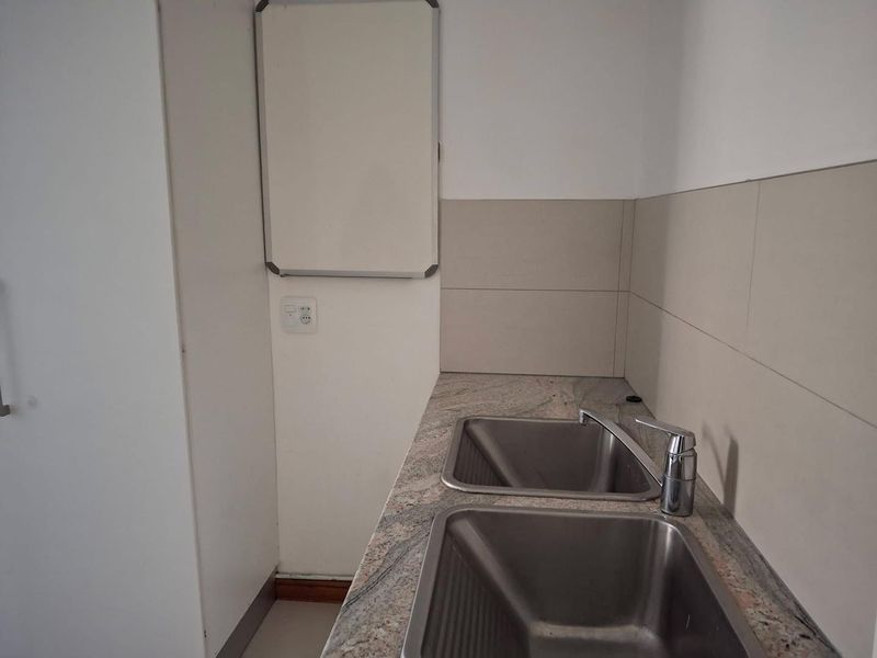 A functional laundry area featuring a double stainless steel sink set into a granite countertop with neutral tiled splashbacks.