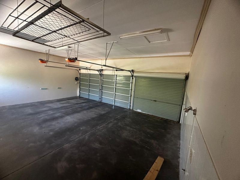 Spacious triple garage featuring concrete flooring, automatic door openers, and a ceiling-mounted drying rack, providing ample storage and parking space.