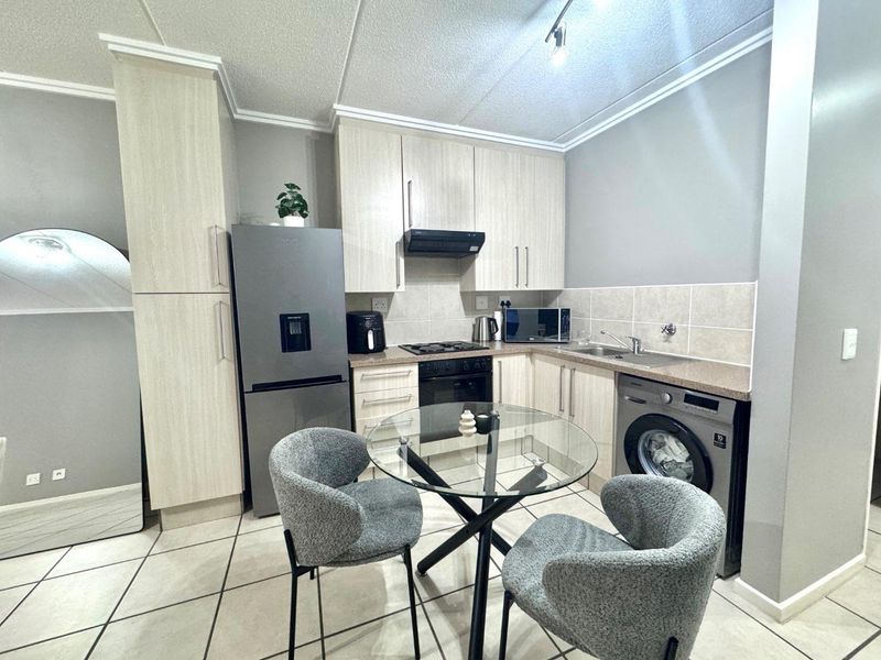 A functional kitchen featuring light wood-finish cabinetry, laminate countertops, a built-in oven with gas hob, and integrated space for laundry appliances.