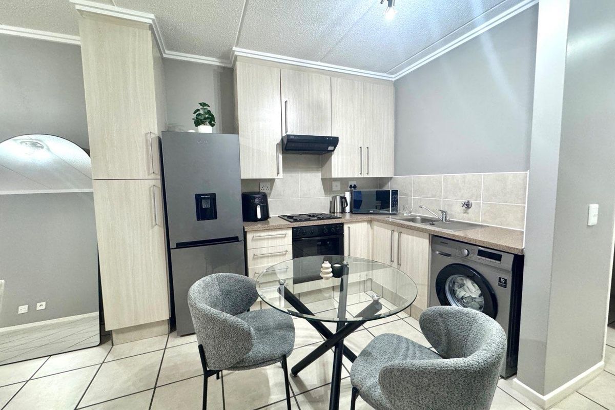 A functional kitchen featuring light wood-finish cabinetry, laminate countertops, a built-in oven with gas hob, and integrated space for laundry appliances.