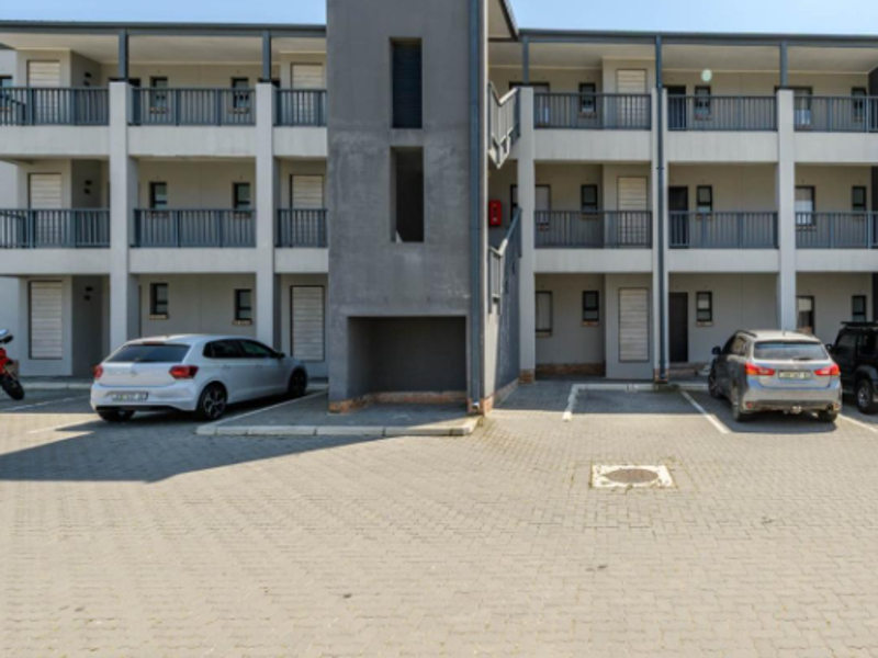 Front elevation of a multi-story apartment complex featuring paved parking, external stairwell access, and private balconies with metal railings.
