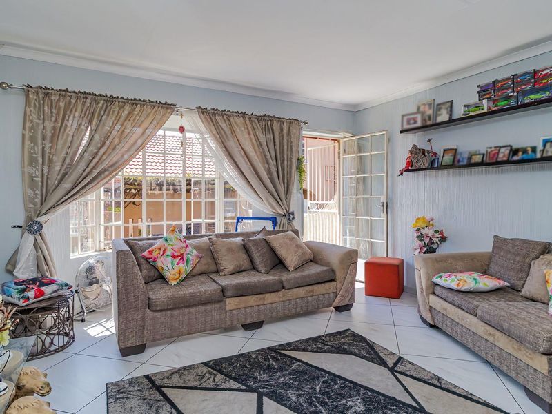 A bright living room featuring tiled flooring, coving, and direct access to the exterior through a security gate and french doors.