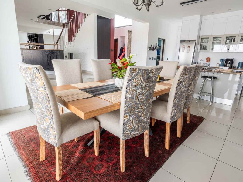 Spacious open-plan dining area featuring tiled flooring, recessed lighting, and an adjacent modern kitchen with built-in cabinetry and a staircase.
