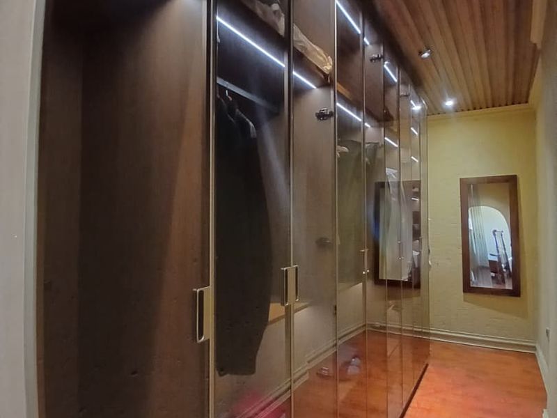 A well-appointed dressing area featuring extensive floor-to-ceiling built-in cupboards with integrated lighting, timber-clad ceiling, and warm laminate flooring.