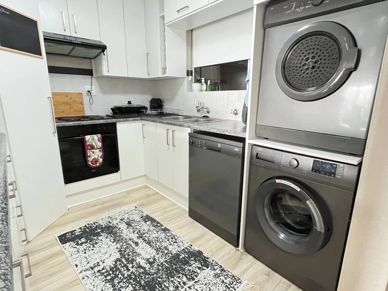Compact kitchen featuring white cabinetry, laminate countertops, built-in oven with extractor fan, and dedicated space for laundry appliances.