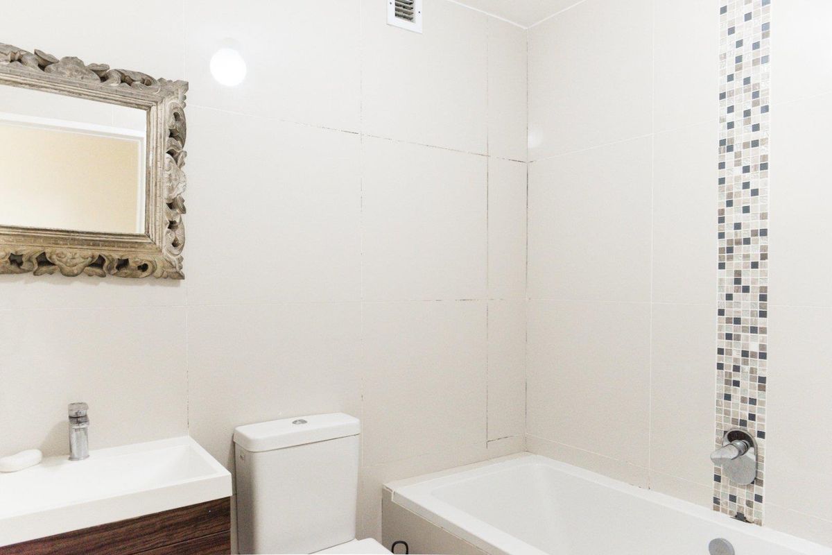 A functional bathroom featuring a white bathtub, a modern vanity with a basin, and a toilet, accented by a decorative mosaic tile feature wall.