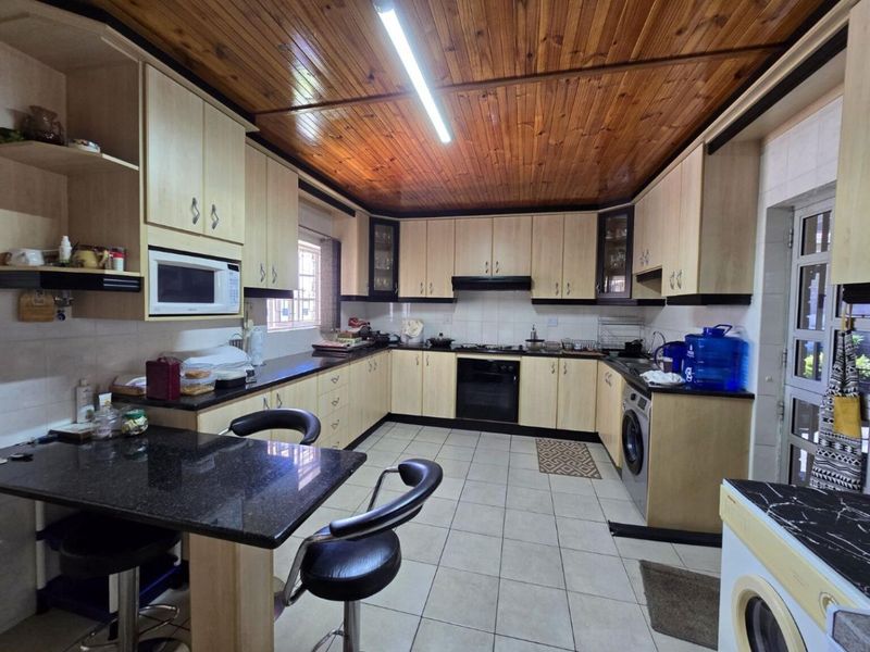 Spacious kitchen featuring extensive built-in cabinetry, granite countertops, integrated appliances, a breakfast nook, and a distinctive timber-paneled ceiling.