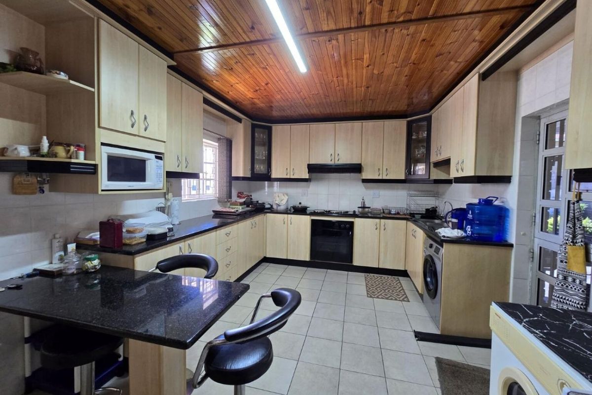 Spacious kitchen featuring extensive built-in cabinetry, granite countertops, integrated appliances, a breakfast nook, and a distinctive timber-paneled ceiling.