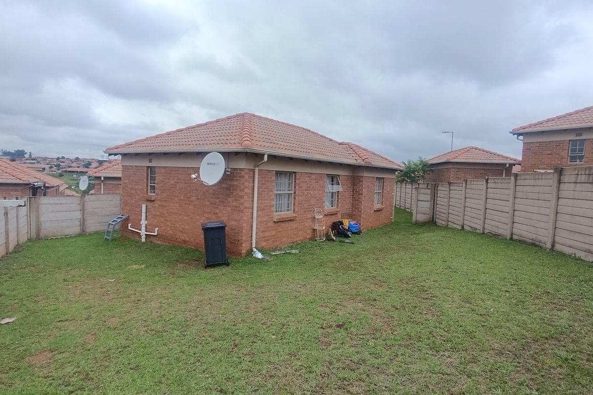A view of the rear exterior of a brick house featuring a tiled roof, perimeter boundary walls, and a private garden area.
