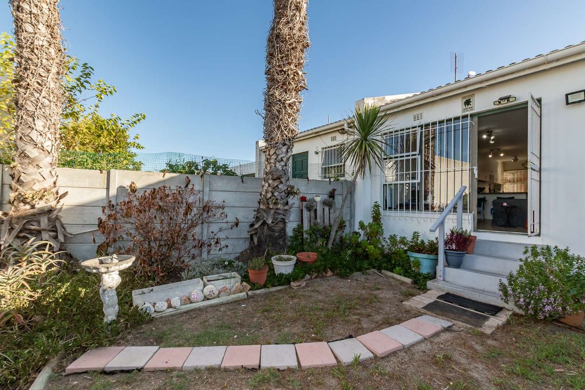 Rear exterior view of the property featuring a small garden area, concrete boundary wall, and access steps leading to the interior.