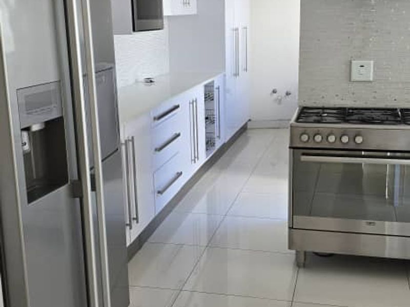 Modern kitchen featuring white cabinetry, stainless steel appliances including a gas stove and extractor fan, mosaic backsplash, and polished tiled flooring.