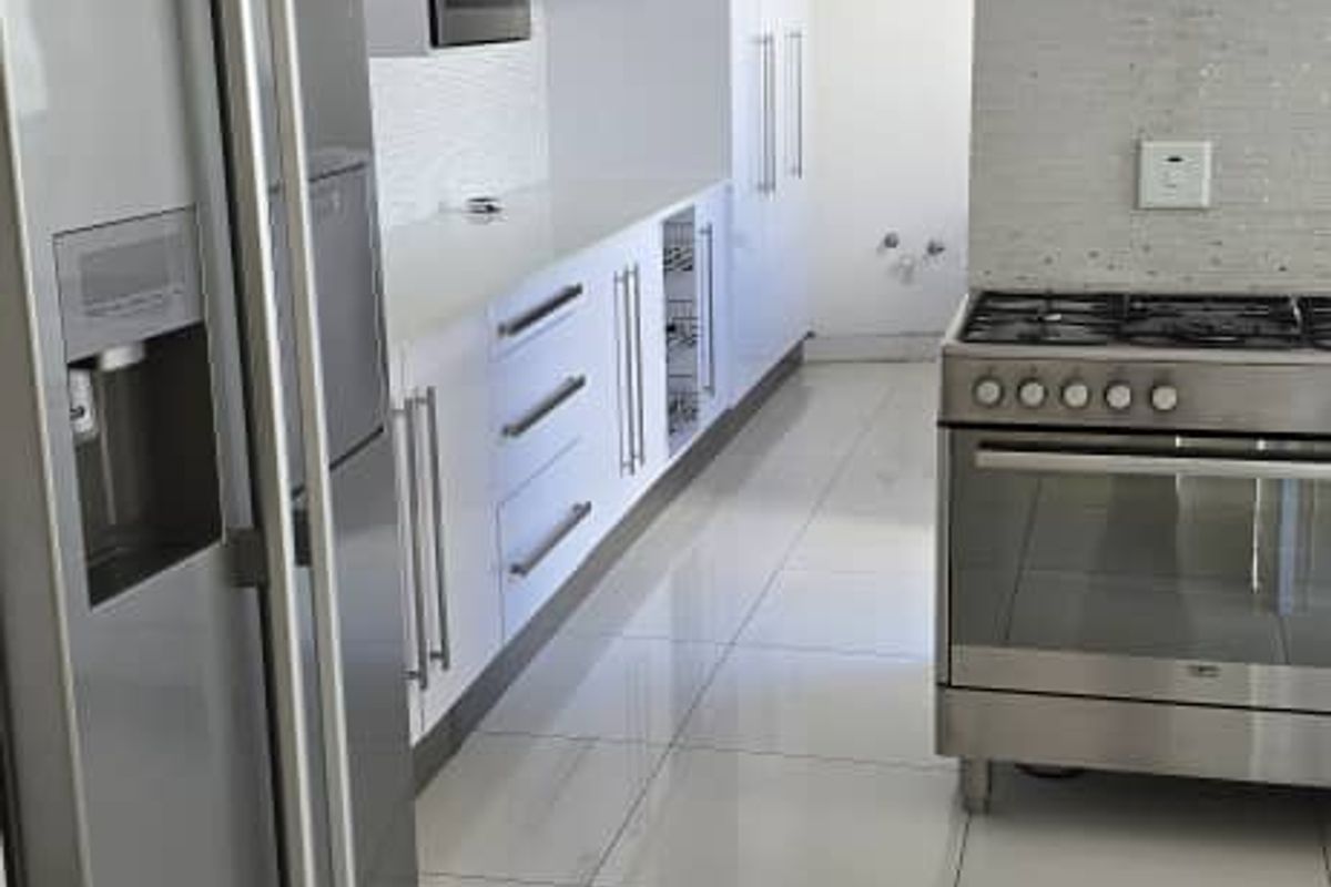 Modern kitchen featuring white cabinetry, stainless steel appliances including a gas stove and extractor fan, mosaic backsplash, and polished tiled flooring.