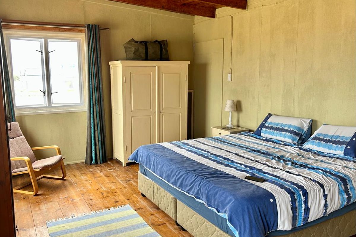 A bedroom featuring exposed timber ceiling beams, timber flooring, and a window providing natural light.