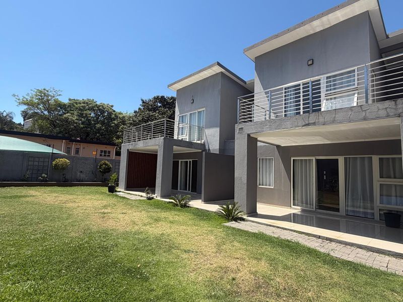 Rear view of a modern double-story cluster home featuring covered patios, upper-level balconies with stainless steel railings, and a spacious private garden.