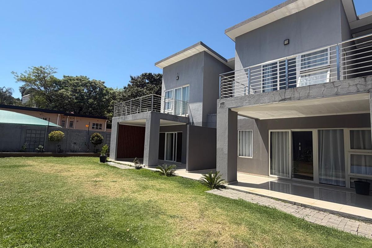 Rear view of a modern double-story cluster home featuring covered patios, upper-level balconies with stainless steel railings, and a spacious private garden.