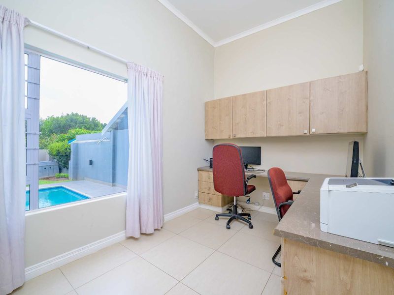 A functional home office featuring built-in cabinetry, a spacious desk, tiled flooring, and a large window overlooking the pool area.