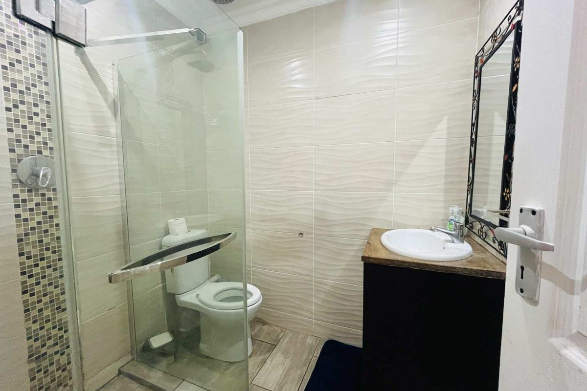 A compact modern bathroom featuring a glass-enclosed shower, tiled walls with textured accents, a vanity basin, and a built-in ceiling extractor fan.