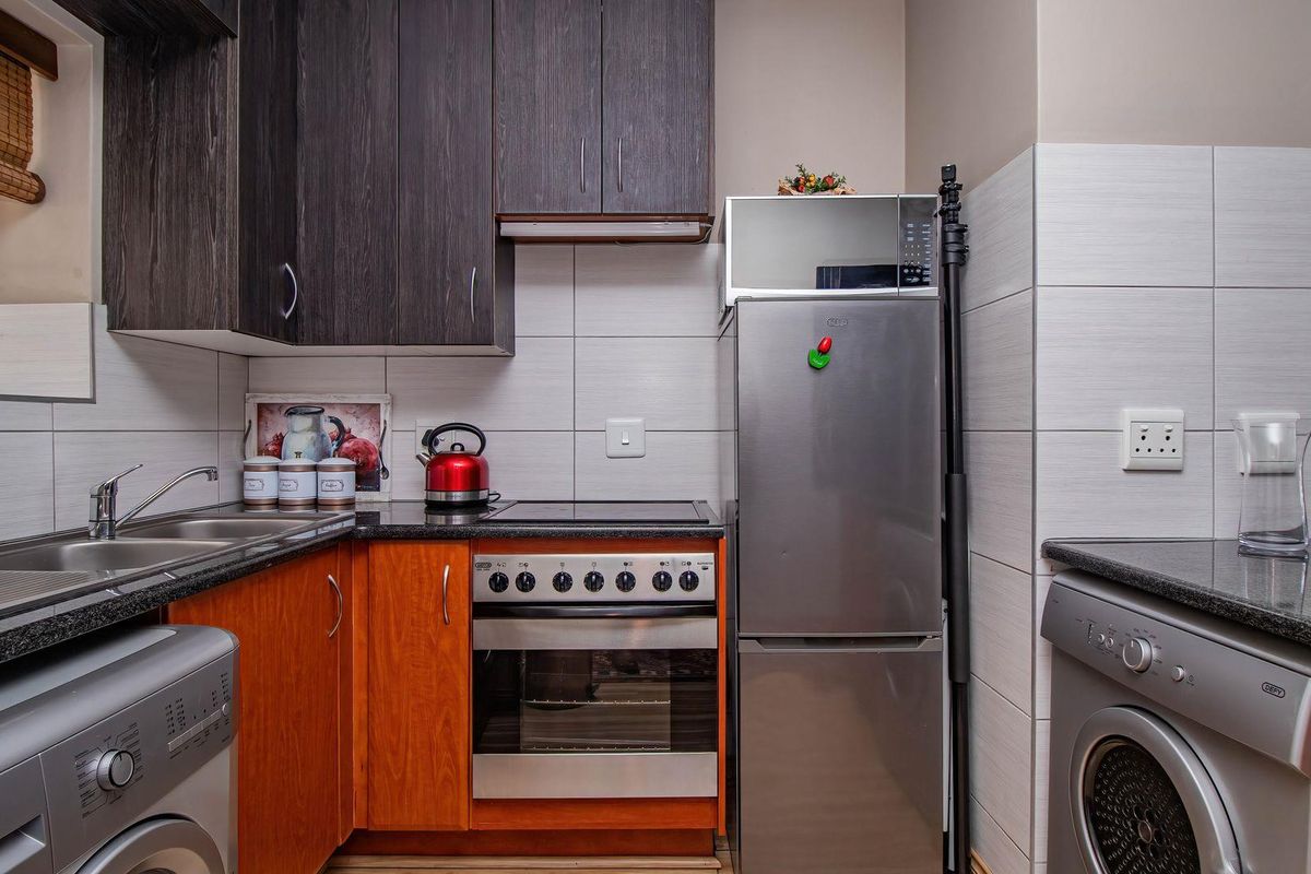 Compact kitchen featuring dark wood upper cabinetry, wood-finish lower cabinets, granite countertops, built-in oven, hob, and integrated laundry appliance space.