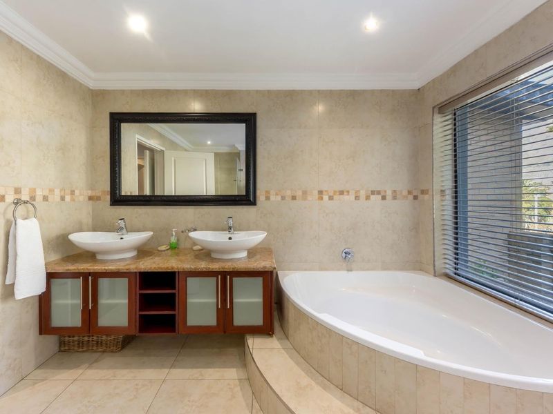 A well-maintained bathroom featuring a double vanity with vessel sinks, a built-in corner bathtub, and neutral wall and floor tiling.